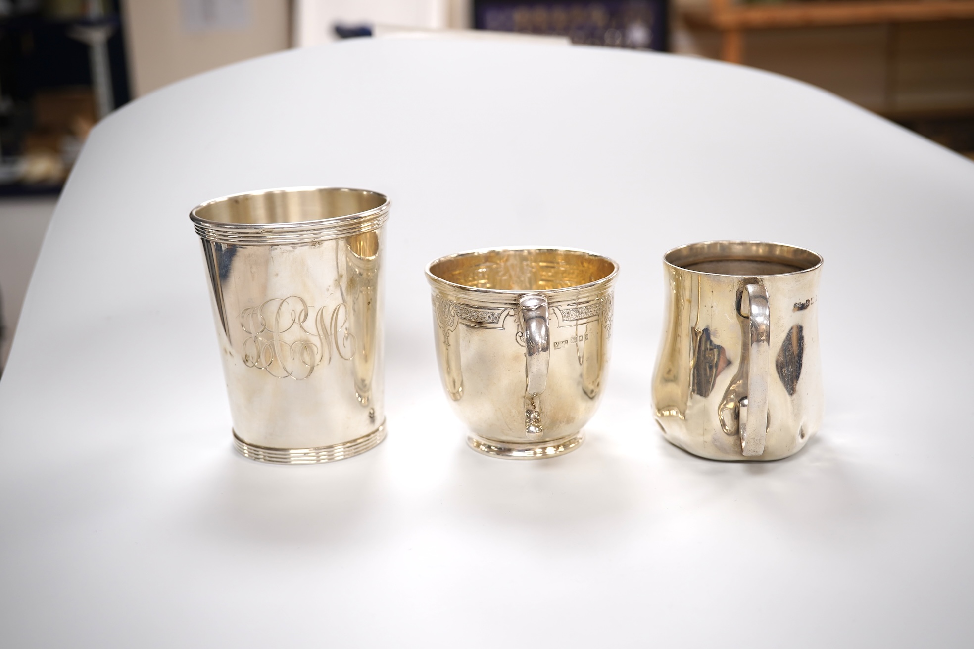 A George V engraved silver tea cup by Mappin & Webb, London, 1924, height 69mm, together with a Gorham sterling beaker and an Edwardian silver christening mug, 11oz.